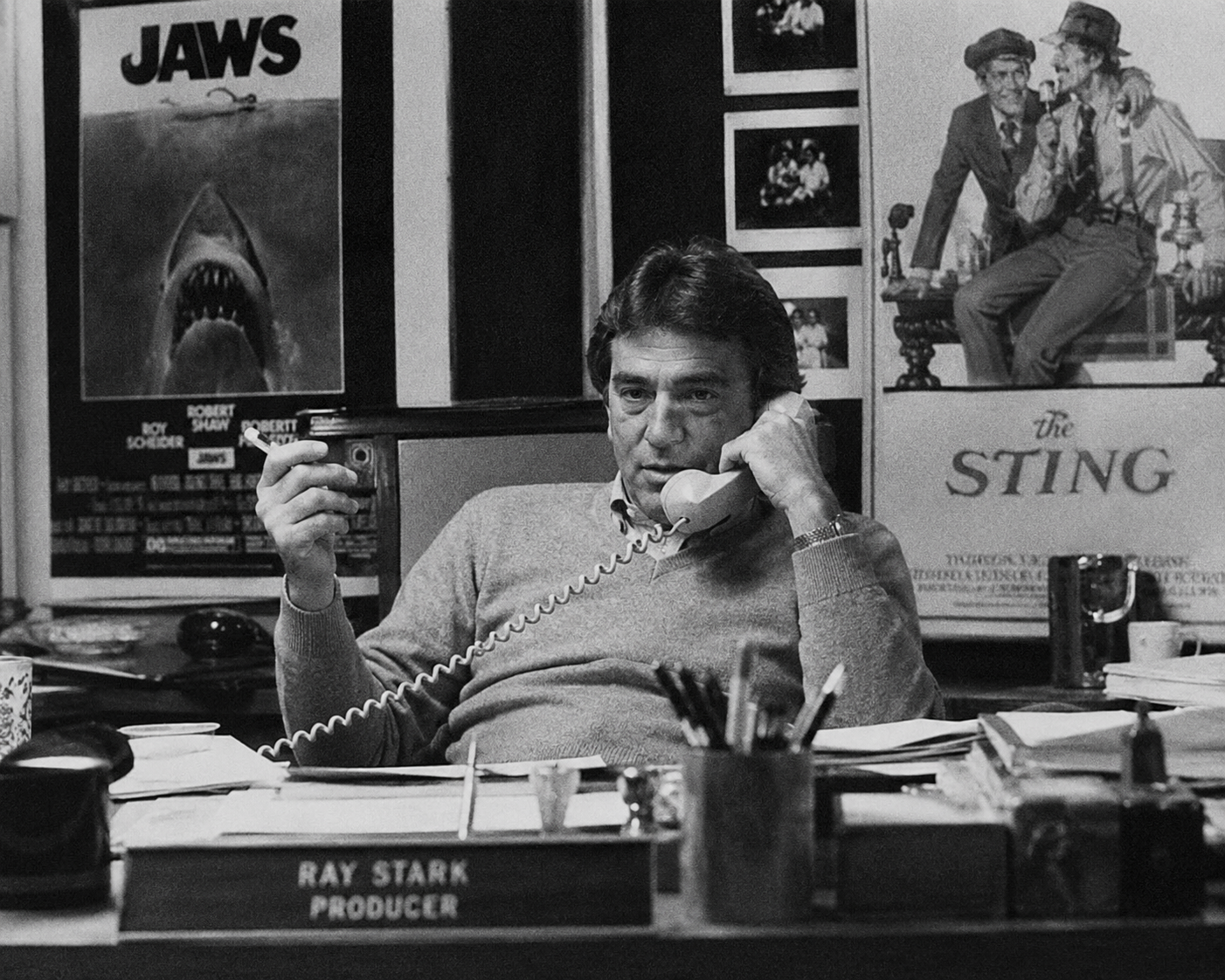 A black-and-white 1980s film crew blocks a scene beside storyboards, a film camera, and a CRT monitor.