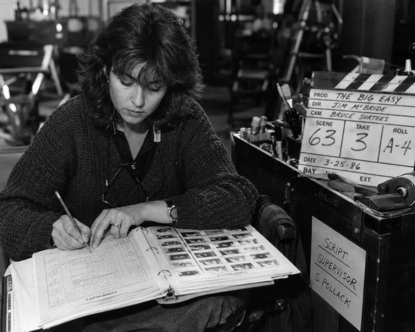 A black-and-white 1980s film crew arranges storyboards, contact sheets, and take strips across an edit bay table.